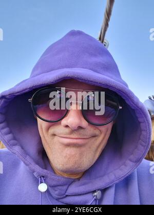 homme souriant avec sweat à capuche violet et lunettes de soleil, portrait Banque D'Images