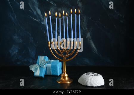 Menorah avec des bougies allumées, des cadeaux et une kippah pour la célébration Hanukkah sur fond sombre Banque D'Images