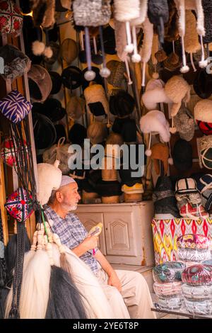 Kashgar, Chine - 17 JUILLET 2022 : homme ouïghour assis dans sa boutique traditionnelle de chapeaux ouïghours dans un marché local dans le vieux Kashgar Banque D'Images