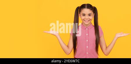 enfant heureux présentant le produit sur l'espace de copie de fond jaune, choix. Visage d'enfant, affiche horizontale, portrait isolé d'adolescente, bannière avec co Banque D'Images