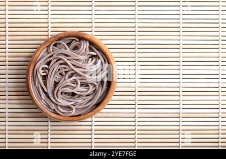 Nouilles soba réfrigérées et bouillies dans un bol en bois placé sur un tapis de bambou. Fines nouilles japonaises, fabriquées principalement à partir de farine de sarrasin, mélangées à de la farine de blé. Banque D'Images