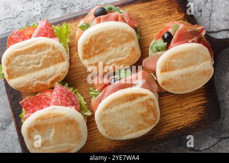 Petits sandwichs italiens tigelle avec saucisse, jamon et légumes frais gros plan sur planche de bois sur table. Vue horizontale de dessus Banque D'Images