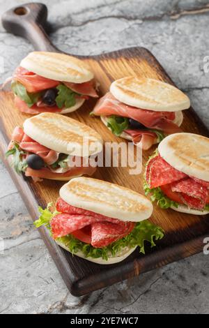 Sandwich Tigella typiquement italien avec salami, jambon et légumes frais gros plan sur planche de bois sur la table. Vertical Banque D'Images