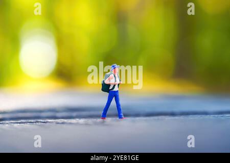 Minuscule figurine d'un routard sur une souche d'arbre, entourée d'un fond vert flou qui évoque un sentiment d'aventure dans la nature. Banque D'Images