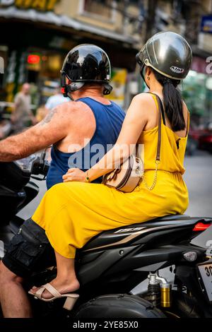 Un homme occidental fait son chemin le long de soi Buakhao, Pattaya Thaïlande avec une jeune dame thaïlandaise à l'arrière du scooter ou du vélo. Banque D'Images