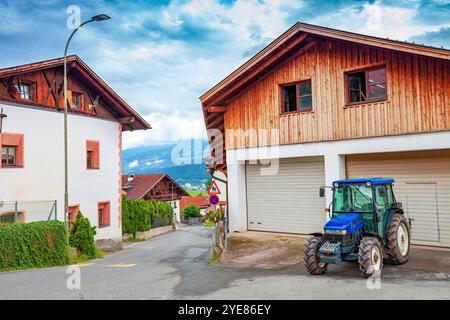 Rue avec fermes et tracteur bleu garé près d'un garage à Innsbruck, Autriche Banque D'Images