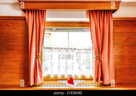 Fenêtre en bois avec de courts rideaux à plis roses pincés et rideau en dentelle dans la maison. Cottage bois fenêtres avec statue ange sur le rebord de la fenêtre Banque D'Images