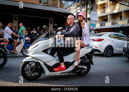 Un homme occidental fait son chemin le long de soi Buakhao, Pattaya Thaïlande avec une jeune dame thaïlandaise à l'arrière du scooter ou du vélo. Banque D'Images