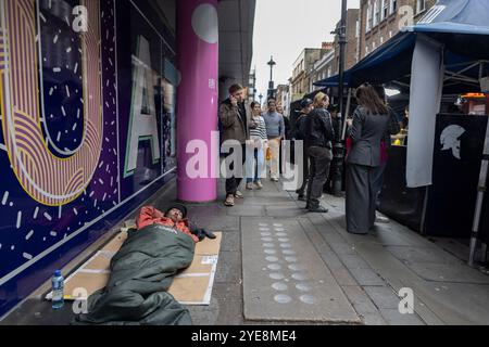 Un sans-abri est allongé dans son sac de couchage sur le trottoir le long du marché de Berwick Street pendant une semaine de travail à l'heure du déjeuner, Soho, Londres, Angleterre, Royaume-Uni Banque D'Images