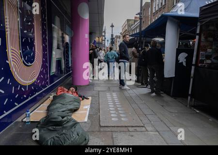 Un sans-abri est allongé dans son sac de couchage sur le trottoir le long du marché de Berwick Street pendant une semaine de travail à l'heure du déjeuner, Soho, Londres, Angleterre, Royaume-Uni Banque D'Images