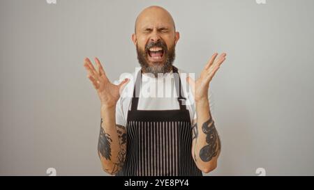 Homme hispanique avec des tatouages dans le tablier criant dans la frustration isolé sur fond blanc Banque D'Images