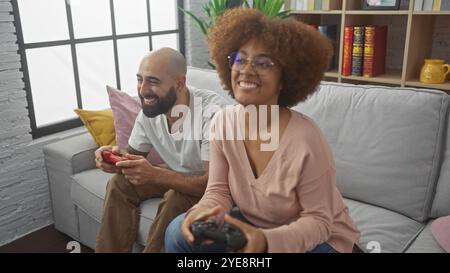 Un joyeux couple interracial profite d'un jeu vidéo ensemble sur un canapé confortable dans un cadre de salon moderne Banque D'Images