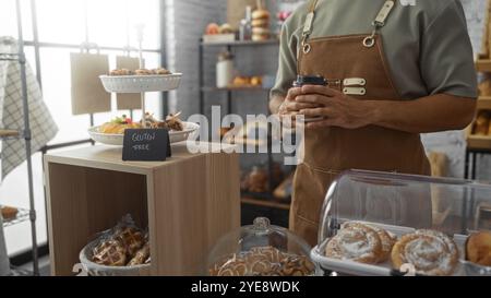 Homme debout à l'intérieur dans une boulangerie tenant une tasse de café avec des pâtisseries sans gluten sur l'affichage Banque D'Images