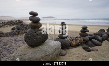 Pierres empilées sur la plage de sable de famara à lanzarote, îles canaries, avec des montagnes lointaines et des vagues océaniques sous un ciel nuageux en plein jour Banque D'Images