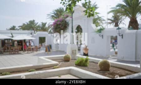 Scène extérieure floue à lanzarote, espagne, avec une arche, des tables, des chaises, bâtiments blancs, plantes et personnes floues, créant un ca flou Banque D'Images