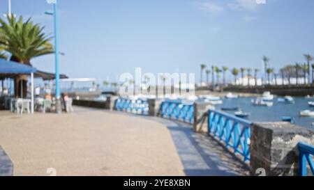 Scène en plein air floue à lanzarote avec des gens déconcentrés profitant d'une journée ensoleillée au bord de l'eau en espagne, avec des palmiers, des bateaux et des rampes bleues Banque D'Images