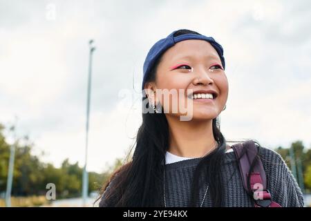 Une jeune étudiante asiatique joyeuse met en valeur son style unique tout en profitant d'une journée en plein air remplie d'énergie. Banque D'Images