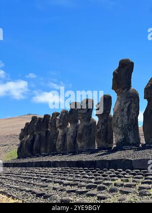 Une ligne de statues moai emblématiques se dresse solennellement sur l'île de Pâques, au Chili, sous un ciel bleu vif. Ces monuments anciens symbolisent le patrimoine Rapa Nui. Banque D'Images