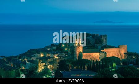 Heure bleue sur Castiglione della Pescaia, la vieille ville illuminée, la mer et l'île de Giglio en arrière-plan. Maremme, région Toscane, Italie, Europe Banque D'Images