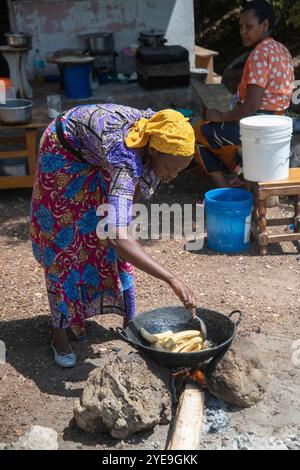 Femme tanzanienne en robe colorée cuisinant des plantains sur un feu ouvert ; MTO wa Mbu, Tanzanie Banque D'Images