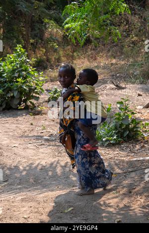 Jeune fille portant son frère sur le dos dans un village près du lac Tanganyika, Tanzanie ; Tanzanie Banque D'Images