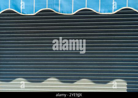 Abstrait Waves Reflections : ombres ensoleillées sur auvent en métal de magasin fermé avec motif rayé. Banque D'Images