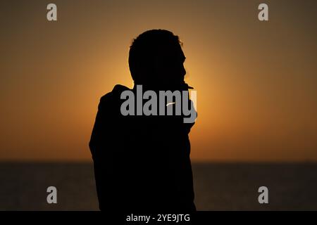 Silhouette d'un homme fumant au bord de la mer Égée au lever du soleil Banque D'Images