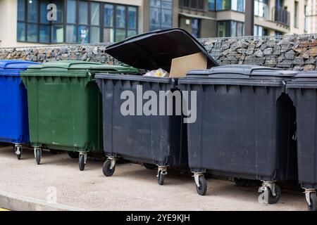 Une rangée soignée de poubelles colorées est alignée devant un grand bâtiment, chacune servant à contenir et éliminer les déchets Banque D'Images