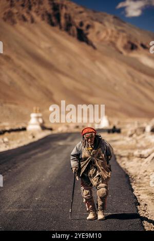 Homme senior marche avec une canne sur une route asphaltée, près de Kurgiakh dans la vallée du Zanskar, Ladakh, Inde ; vallée du Zanskar, Ladakh, Inde Banque D'Images