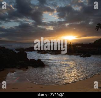 Couple silhouetted se tient sur un rocher dans un rayon de soleil profitant du coucher de soleil d'une île hawaïenne ; Hawaii, États-Unis d'Amérique Banque D'Images