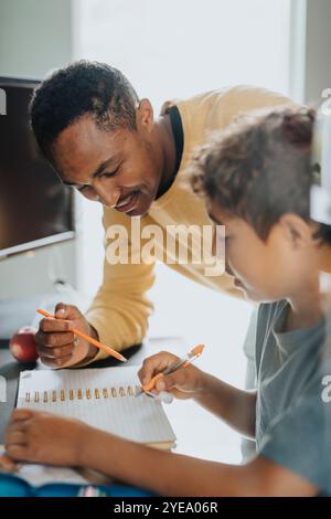Père souriant aidant son fils à faire ses devoirs à la maison Banque D'Images