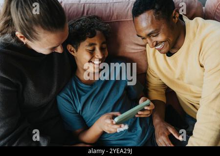 Vue en angle élevé des parents assis sur le canapé à côté du fils à l'aide d'un téléphone intelligent Banque D'Images