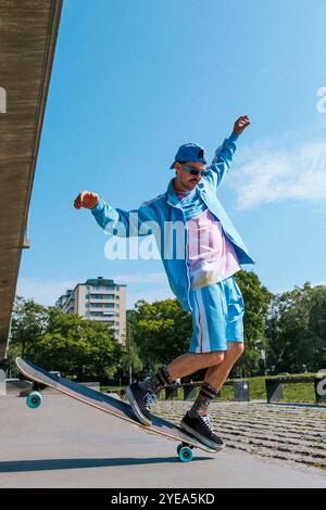 Jeune homme à la mode longboard patinant sur la route de passage supérieur sous le ciel bleu Banque D'Images