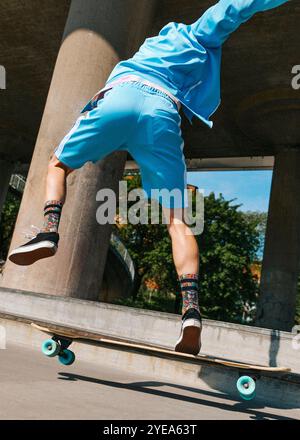 Vue à angle bas de l'homme athlétique longboard patinant sur la route de passage supérieur à la journée ensoleillée Banque D'Images