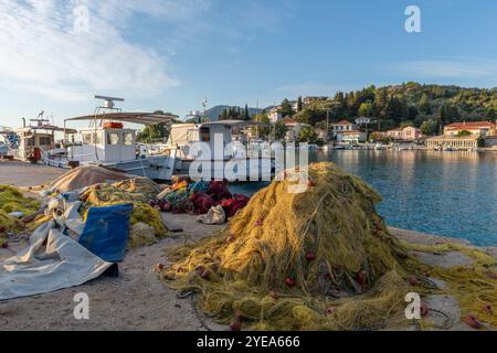 Séchage des filets de pêche sur la jetée du port avec bateau de pêche traditionnel et une vue sur le bâtiment en bord de mer du village de Lygia, île de Lefkada, Grèce. Banque D'Images