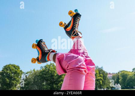 Section basse de la femme portant des patins à roulettes rayés arc-en-ciel sous le ciel bleu Banque D'Images