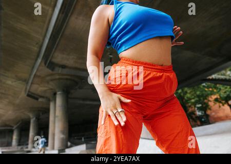 Section médiane d'angle bas de la jeune femme en haut bleu posant près du passage supérieur Banque D'Images