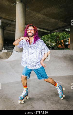 Heureux jeune homme avec les cheveux teints posant tout en patinant à roulettes sur la route de passage supérieur sous le pont Banque D'Images