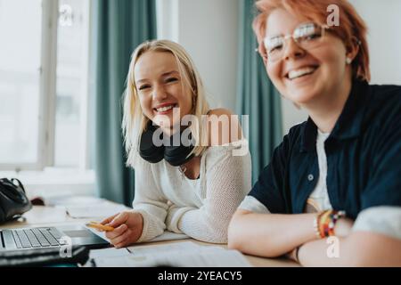 Portrait de fille blonde heureuse et personne non binaire assise au bureau dans la salle de classe Banque D'Images