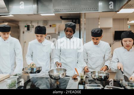 Stagiaires masculins et féminins avec des casseroles préparant des aliments à l'école culinaire Banque D'Images