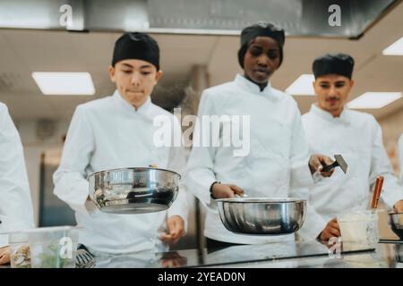 Stagiaires masculins et féminins avec des casseroles préparant la nourriture tout en travaillant dans la cuisine commerciale Banque D'Images