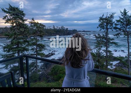 Vue prise de derrière une femme en peignoir regardant l'océan sans fin depuis un balcon à Ucluelet ; Île de Vancouver, Colombie-Britannique Banque D'Images