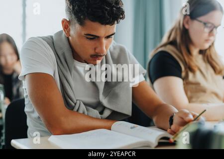 Adolescent garçon lisant le livre tout en étant assis par la fille dans la classe Banque D'Images