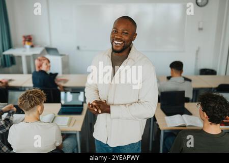 Portrait d'un enseignant masculin heureux debout au milieu des élèves assis au bureau dans la salle de classe Banque D'Images