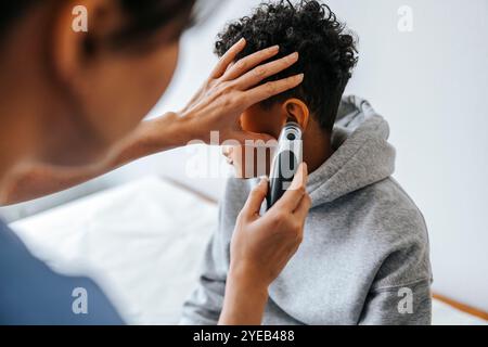 Pédiatre féminin vérifiant l'oreille du garçon avec thermomètre dans la salle d'examen médical Banque D'Images