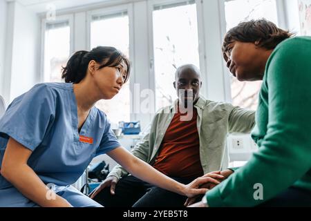 Triste travailleuse de santé consolant une patiente âgée assise à côté de son fils dans la salle d'examen Banque D'Images