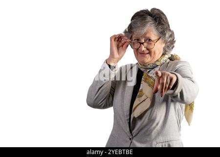 Portrait de femme âgée excitée pointant vers quelque chose sur fond blanc. Femme caucasienne mature avec des lunettes et une veste grise regardant le point de la caméra Banque D'Images