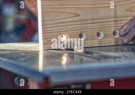 Grande planche de bois avec trous ronds dans l'atelier de menuiserie. Scie circulaire. Main de charpentier. Couper Banque D'Images