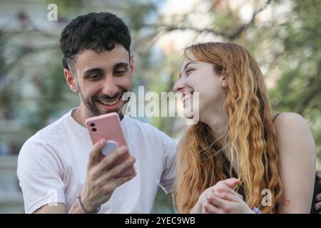 portrait de jeune couple joyeux utilisant un téléphone portable à l'extérieur Banque D'Images