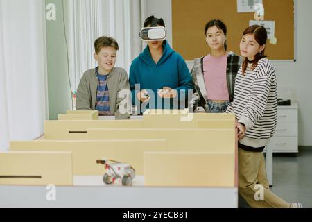 Garçon en sweat à capuche bleu profond avec casque VR entouré de ses camarades de classe jouant au jeu vidéo Banque D'Images